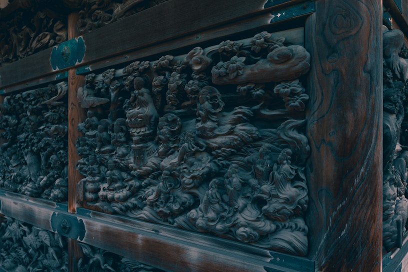Elaborate wooden carvings with intricate designs featuring mythical and nature motifs. The carvings appear detailed with swirling patterns and figures, possibly depicting a scene involving animals and deities.