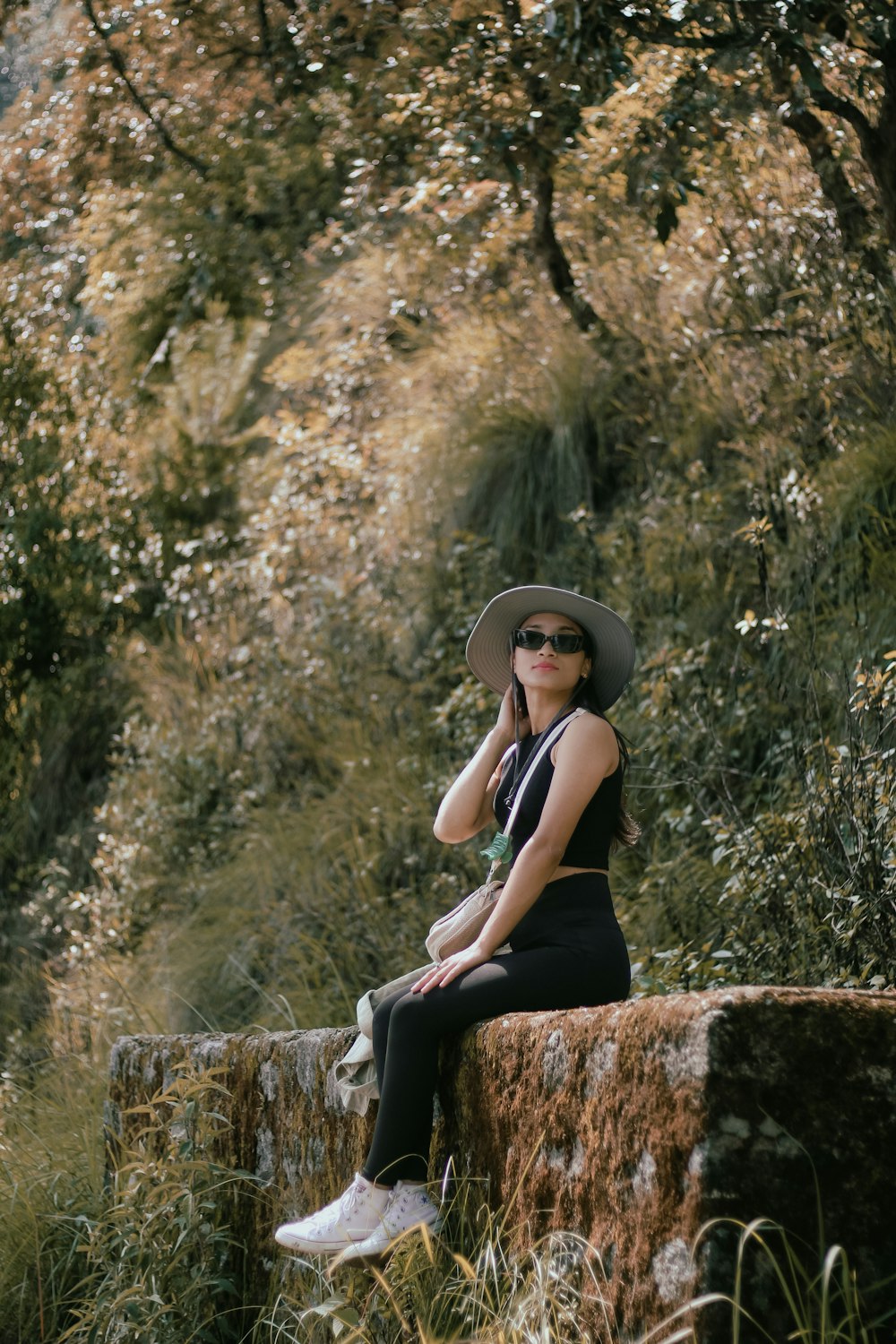 a woman wearing a hat and sunglasses sitting on a rock