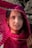 A woman is gazing upward while holding a vibrant pink shawl with a striped pattern over her head. Sunlight filters through the material, casting a patterned shadow across her face. She appears to be in a contemplative or peaceful mood, with natural light accentuating her facial features.