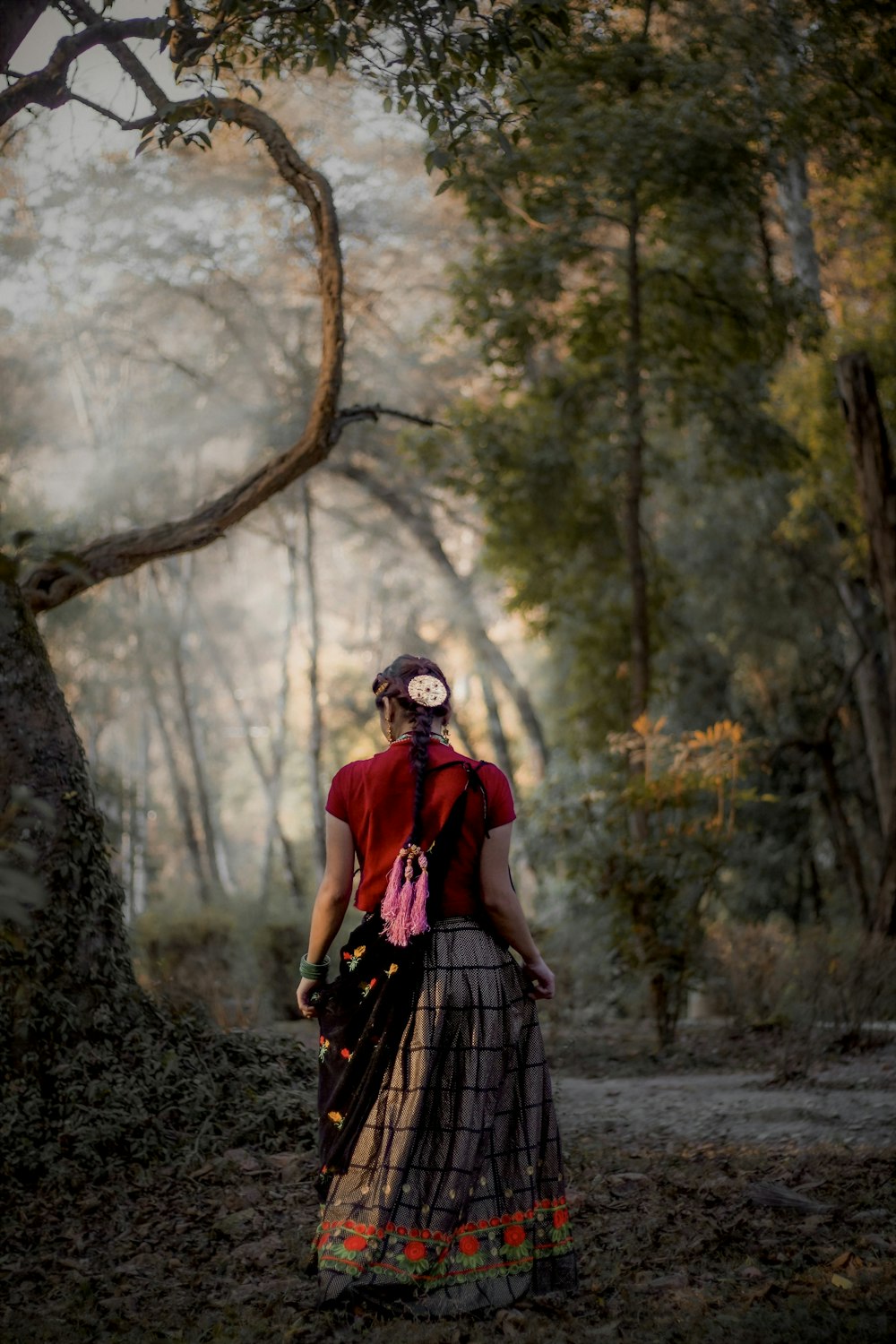 a woman in a red shirt and a plaid skirt standing in a forest