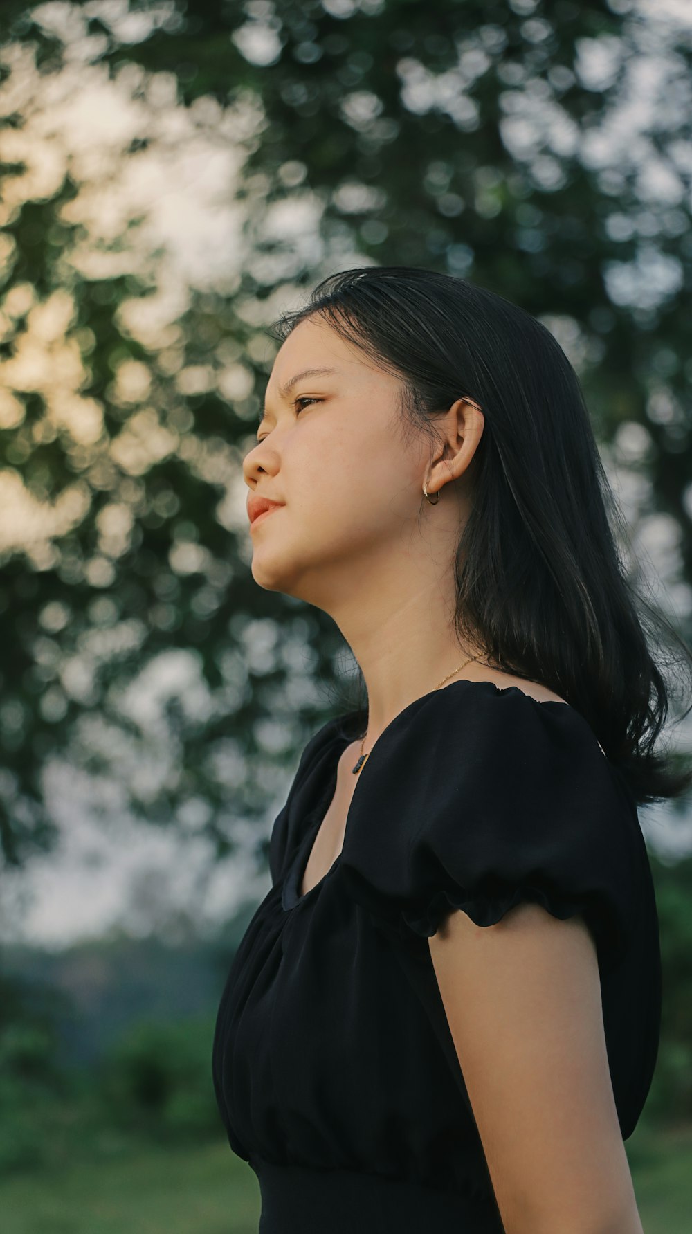 a woman in a black dress standing in front of a tree