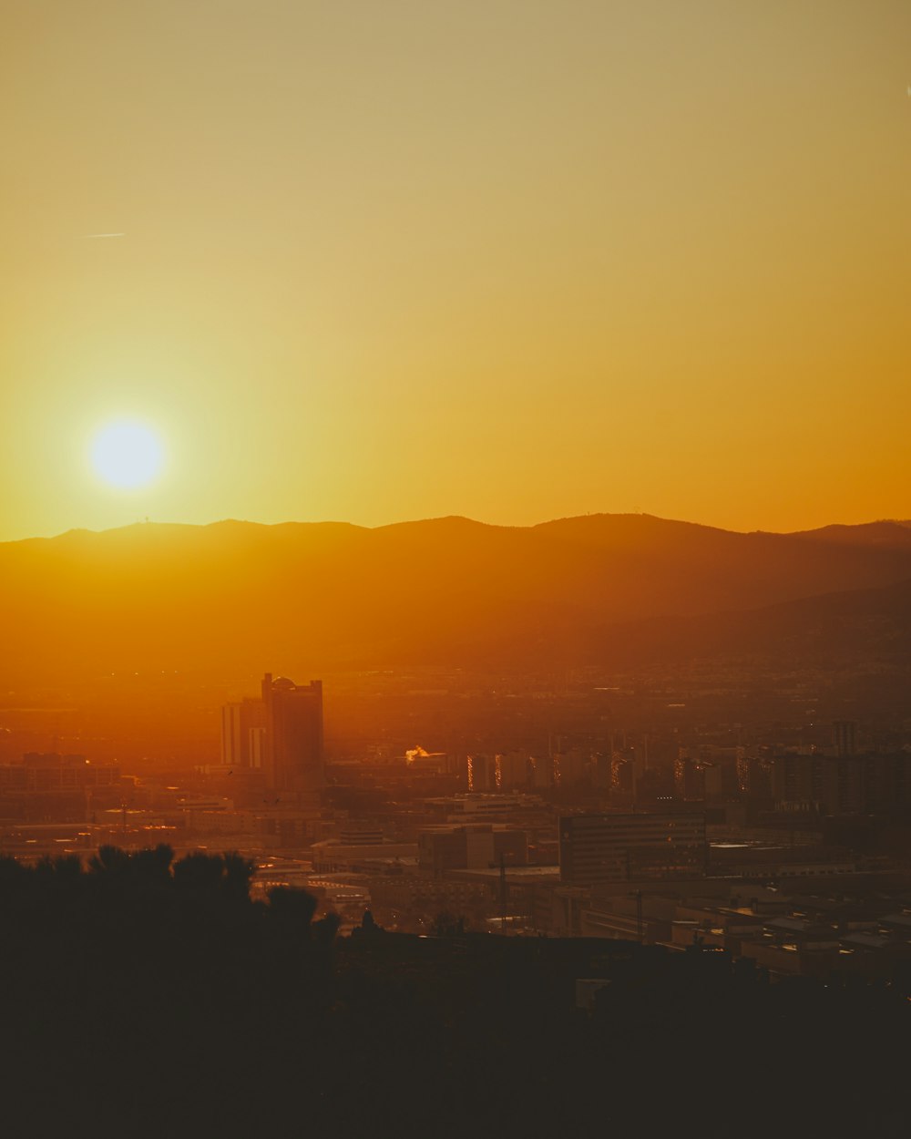 the sun is setting over a city with mountains in the background