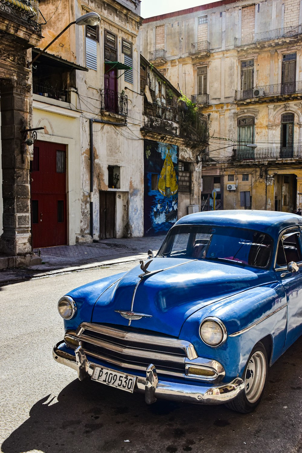 an old blue car parked on the side of the road