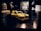 A model car with a glossy yellow finish and black stripes is placed on a dark surface. The car doors are open, revealing some interior details. The background is blurred and dark, creating a dramatic contrast with the vibrant model car.