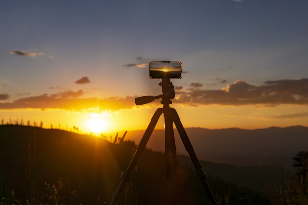 a camera on a tripod with the sun setting in the background