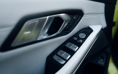 Close-up view of a car's interior door panel featuring multiple buttons, including window controls and a door handle. The panel has a modern design with sleek lines and a mix of materials like plastic and metal.