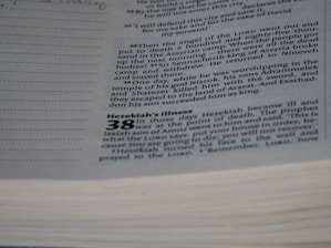 A close-up view of a page from a book with text printed on it. The text appears to be a passage from a biblical or religious text, discussing events involving Hezekiah and a prophet named Isaiah. The page has a section header that reads 'Hezekiah’s Illness' and includes numbered verses and additional lines for notation.