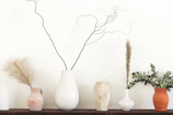 Organic vases with dried grasses placed on a sand-toned shelf against a warm white wall.