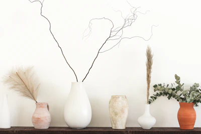 Organic vases with dried grasses placed on a sand-toned shelf against a warm white wall.