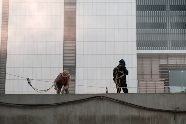 Construction workers collaborating on a modern building site with red and gray safety gear.