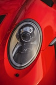 A close-up view of a shiny red car's headlight, showcasing sleek and modern design elements with reflections on the surface.