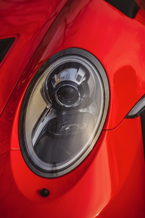 A close-up view of a shiny red car's headlight, showcasing sleek and modern design elements with reflections on the surface.