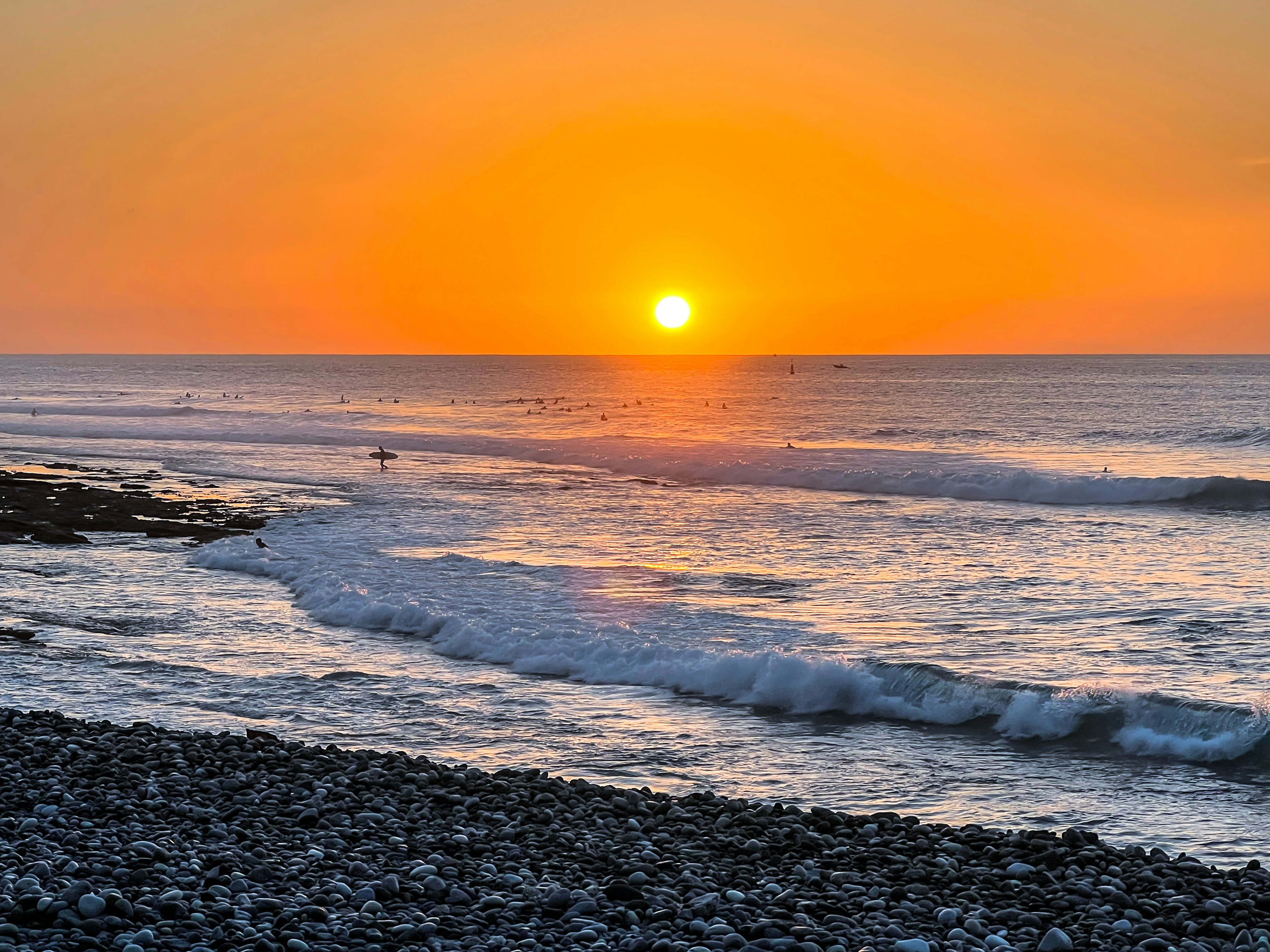 a sunset over the ocean with a surfer in the water