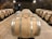 A dimly lit cellar with rows of wooden barrels lined neatly on both sides. The barrels are set on racks over a gravel floor. The walls and ceiling are made of stone, giving the atmosphere an old-world charm.
