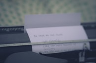 A close-up of a typewriter with a sheet of paper halfway typed, resting on a wooden table with scattered autumn leaves.