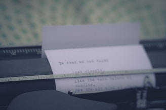 A close-up of a typewriter with a sheet of paper halfway typed, resting on a wooden table with scattered autumn leaves.
