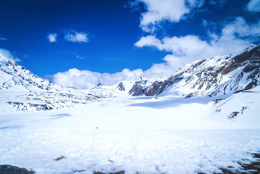 a snow covered mountain range under a cloudy blue sky