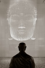 A serene monk meditating in front of a softly glowing screen displaying Buddha Dhamma teachings.