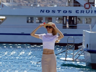 a woman in a skirt and a hat standing in front of a boat