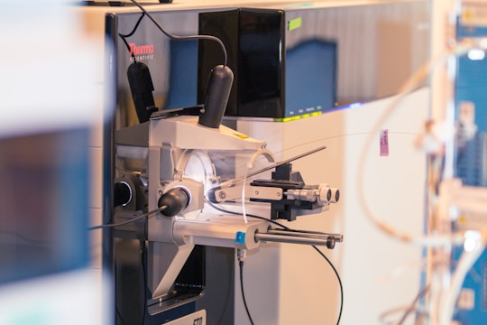 A complex scientific instrument, likely a mass spectrometer, is positioned in a laboratory setting with various probes and wires connected to it. The machine features the brand name Thermo Scientific, indicating its use in scientific research or analysis.
