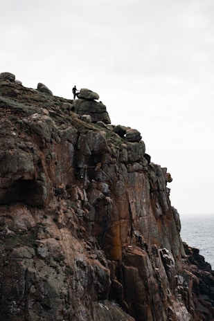 A cloaked figure standing on a rocky cliff, overlooking a stormy sea under a thunderous sky.