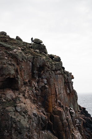 A dramatic scene of a lone figure standing on a cliff edge under a stormy sky, emphasizing mood and scale.