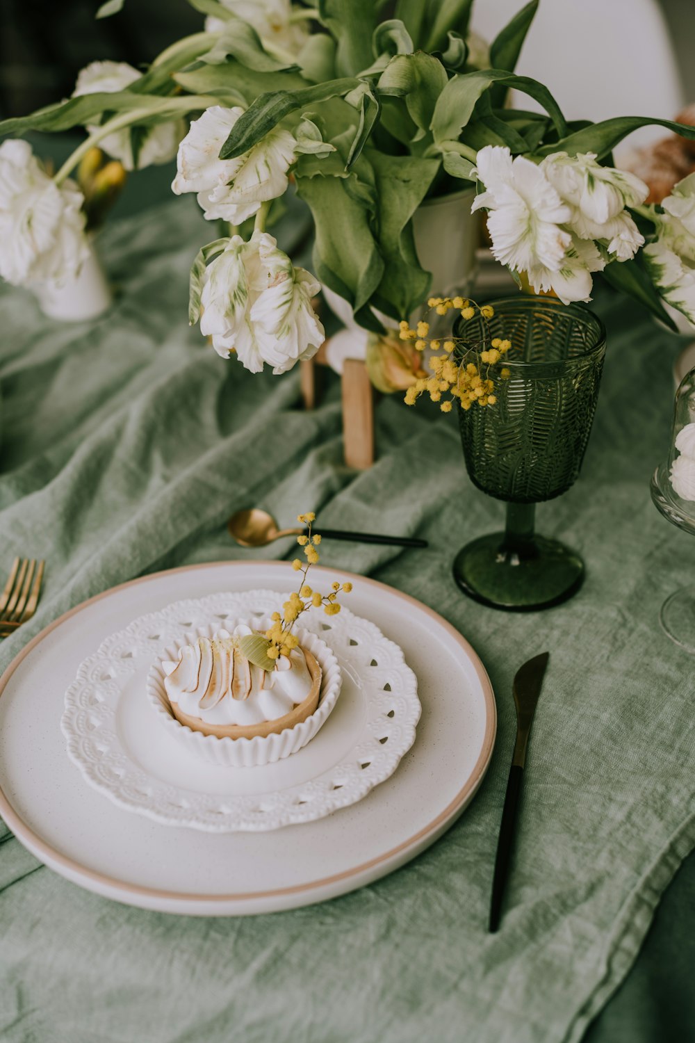 a white plate topped with a pastry next to a vase of flowers