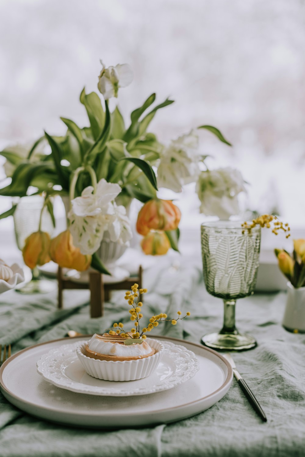 a white plate topped with a cupcake next to a vase of flowers