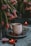 A cozy and intimate setting featuring a white mug with a hole pattern sitting on a gray plate, surrounded by fresh raspberries. Bright pink tulips drape over, adding a touch of natural beauty. Heart-shaped candles and a lollipop enhance the romantic ambiance.