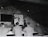 A group of men in military uniforms are gathered in a rustic attic-like room, where they seem to be engaged in a lesson or lecture. One man stands at the front, pointing at an anatomical chart displayed on the wall, while the others are seated at benches, attentively observing.