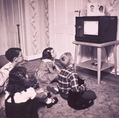 Children gathered around a small screen watching an educational broadcast in a remote village.