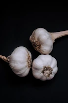 Close-up of glossy black garlic bulbs arranged on rustic wooden table in natural light.