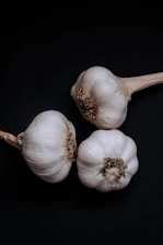 Close-up of glossy black garlic bulbs arranged on rustic wooden table in natural light.