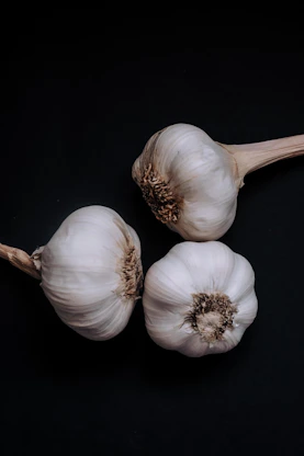 Close-up of glossy black garlic bulbs arranged on rustic wooden table in natural light.