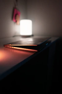 A sleek, minimal table lamp casting warm light on a clean, modern desk setup in a softly lit room.