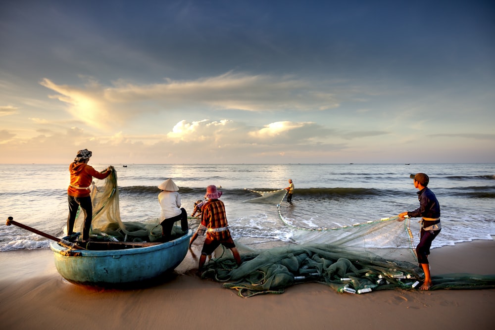 um grupo de pessoas em pé no topo de uma praia ao lado de um barco