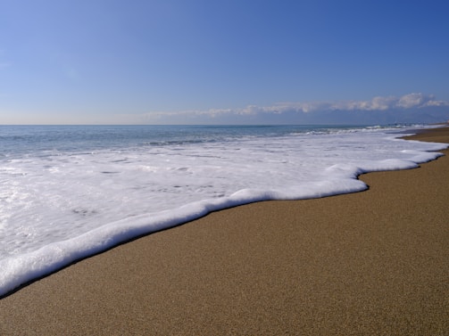 A serene ocean wave gently rolling onto a sandy beach under a clear blue sky.