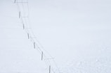A long fence stretches diagonally across a vast, snow-covered landscape. The fence consists of wooden posts connected by wire.
