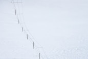 A long fence stretches diagonally across a vast, snow-covered landscape. The fence consists of wooden posts connected by wire.