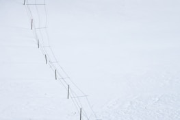 A long fence stretches diagonally across a vast, snow-covered landscape. The fence consists of wooden posts connected by wire.