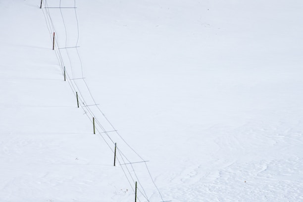 A long fence stretches diagonally across a vast, snow-covered landscape. The fence consists of wooden posts connected by wire.