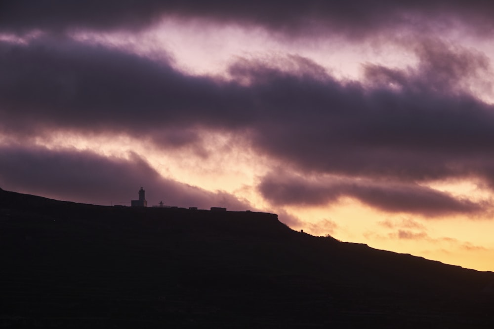 a hill with a lighthouse on top of it under a cloudy sky