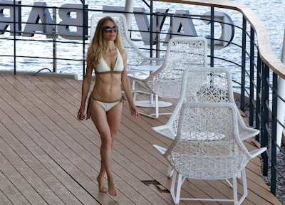 A model walking along a tropical resort pool wearing a flowing white beach cover-up.