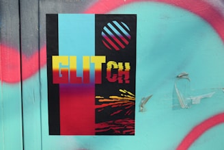 A poster features bold text reading 'GLITCH' against a black background divided by vertical stripes in cyan and red. Above the text, a circle with diagonal stripes in cyan and red is depicted. The lower section has a glitch effect with yellow, red, and black colors blending. This is placed on a textured surface with turquoise paint and irregular red spray-painted lines.