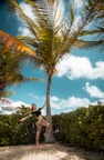 a woman standing next to a palm tree on a beach