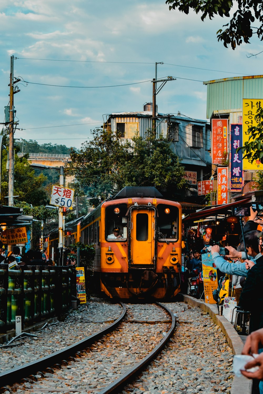 a yellow train traveling down train tracks next to a crowd of people