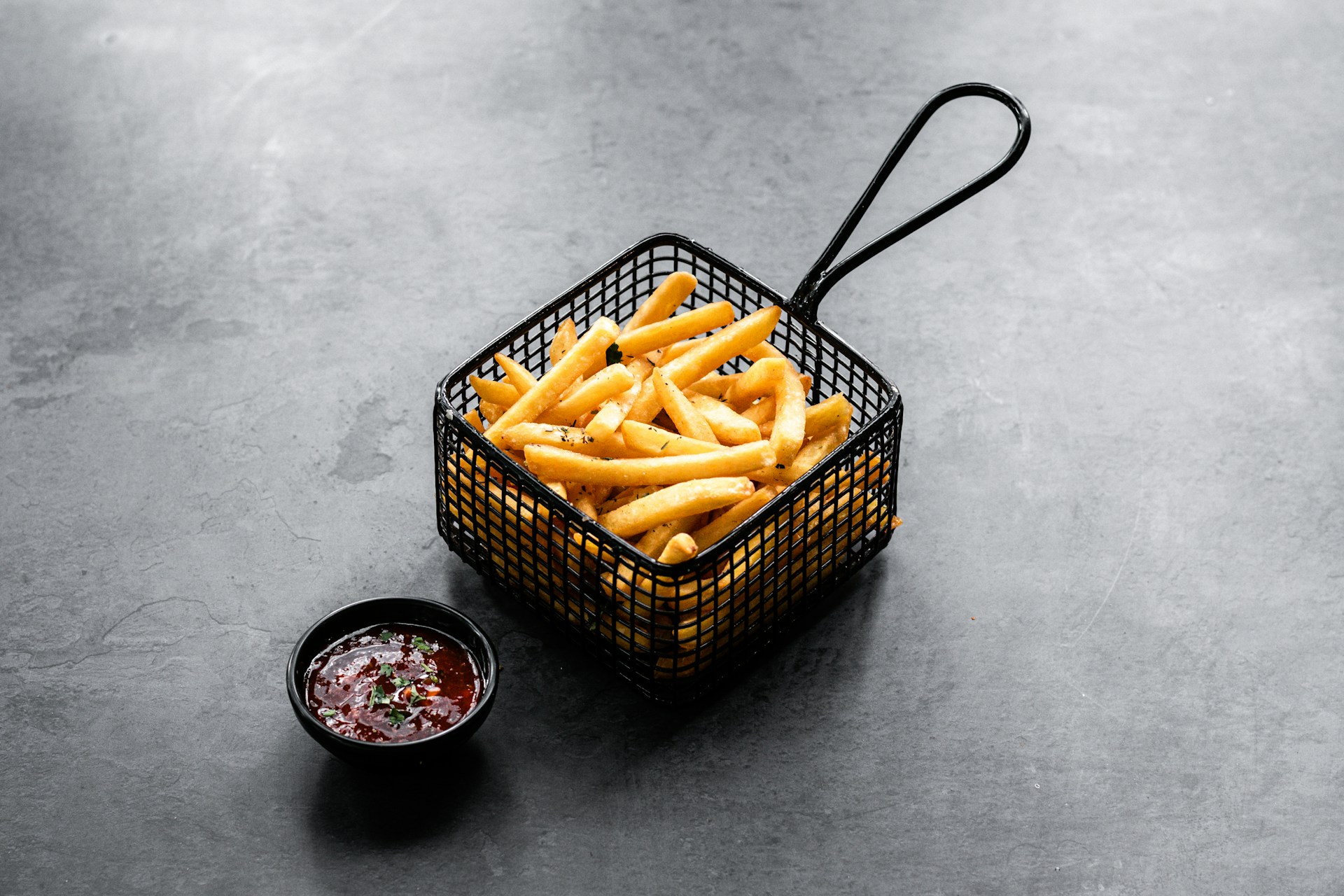 A vibrant display of golden, crispy French fries served in a rustic basket with a side of tangy dipping sauce, highlighting the warm and inviting atmosphere of the panchería.