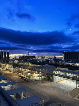 A sprawling industrial refinery complex at dusk with illuminated pipelines and storage tanks.