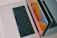Two laptops are placed side by side on a light-colored wooden surface. One laptop is partially open, and the other is lying flat. The open laptop's screen reflects bright orange, blue, and yellow hues, suggesting a vibrant graphical display. Both laptops have black keyboards.