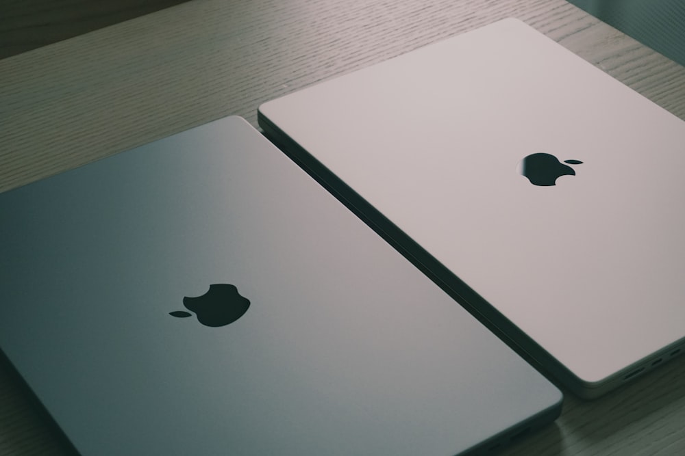 two apple laptops sitting side by side on a table